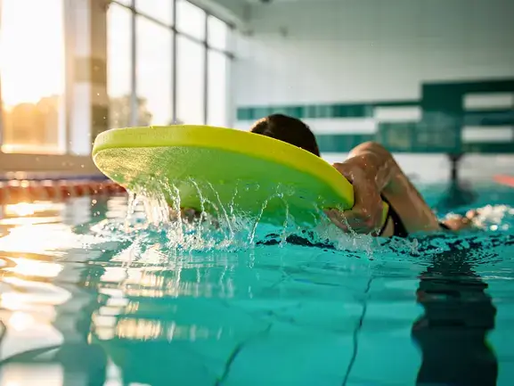 Beginner swimmer practicing with a kickboard in a lap pool, focusing on form and splash.