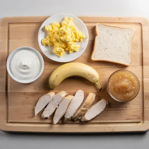 Assortment of low-fiber, soft foods like yogurt, eggs, banana, and applesauce on a wooden board.